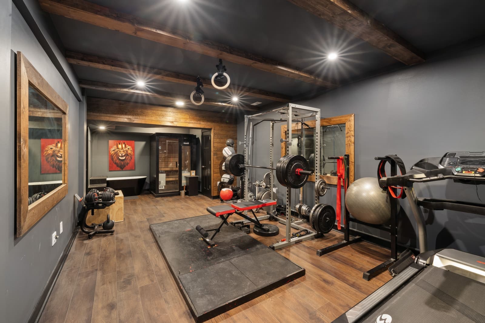 A home gym room with a treadmill and free weights set up against a wall